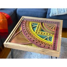 a wooden table with an intricate design on it in front of a blue couch and red throw pillow