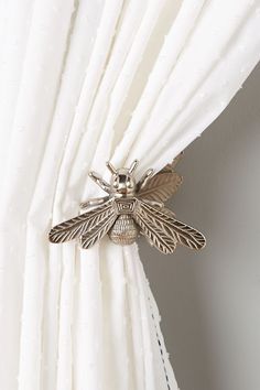 a close up of a white curtain with a silver bee on the back of it