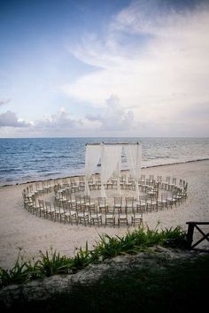 an outdoor ceremony setup on the beach with white drapes and chairs set up to look out over the ocean