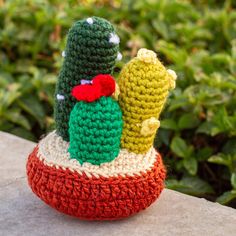 a crocheted cactus sitting on top of a red and green pot filled with cacti