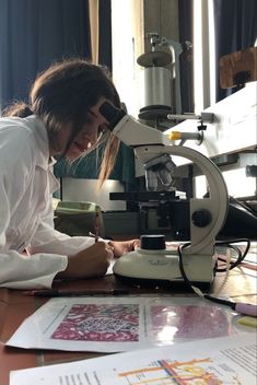 a woman sitting at a table in front of a microscope and writing on a piece of paper