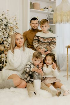 a family sitting on the floor in front of a christmas tree with their two children