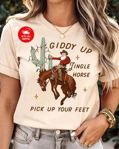 Cowboy Christmas T-Shirt, Giddy Up Jingle Horse Pick Up Your Feet, Cowgirl Shirt, Christmas Shirt, Howdy Country Christmas Horse, Cowboy Tee 🌟 Welcome to Custom Style Lab Art! 🌟 We're thrilled to have you here! Thank you for stepping into our store, where you'll discover carefully crafted, high-quality products. Our unique gift options are perfect for surprising your loved ones, friends, family, and colleagues. Each design is created to bring a smile to their faces! Why Choose Us? Our prints are produced using state-of-the-art DTF machines, ensuring bright colors and exceptional quality. Each order is crafted with premium materials to bring your vision to life. Every product you purchase is important to us--we want to accompany you in your most beautiful moments with our high-quality off Lab Art, Horse Cowboy, Horse Graphic, Christmas Horse, Chain Scarf, Christmas Horses, Boho Cowgirl, Kimono Sweater, Cowboy Christmas