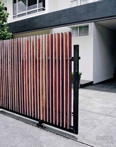 an iron gate with wooden slats on the side of a building next to a tree