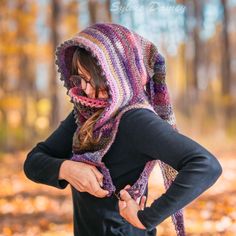 a woman wearing a crocheted hood and scarf in the woods with her hands on her hips