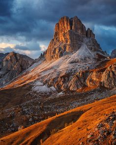 the mountains are covered in snow and brown grass, under a dark sky with clouds