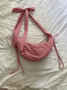 a red and white checkered handbag tied to a string on top of a bed