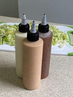 two bottles filled with liquid sitting on top of a counter next to a plate full of lettuce