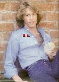 a man sitting against a brick wall holding a cup