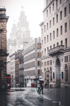 two people walking down the street in the rain with an umbrella and clock tower behind them