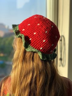 a woman with long hair wearing a crocheted strawberry hat looking out the window