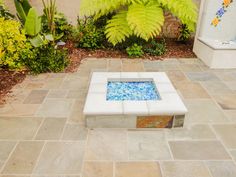 a white bench sitting on top of a stone floor next to a lush green plant