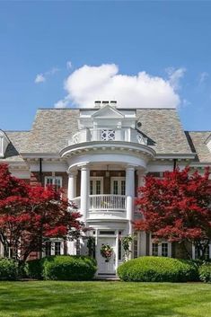 a large white house with red trees in the front yard