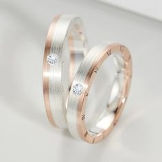 two white and rose gold wedding bands with diamond inlays on each band, set against a plain background