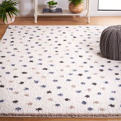 a white rug with blue and brown flowers on it in front of a potted plant