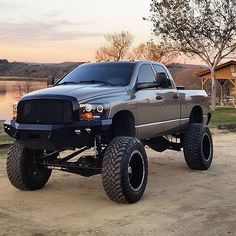 a large gray truck parked on top of a dirt road next to a lake at sunset