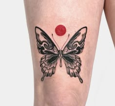 a black and white butterfly tattoo on the thigh with a red dot in the middle