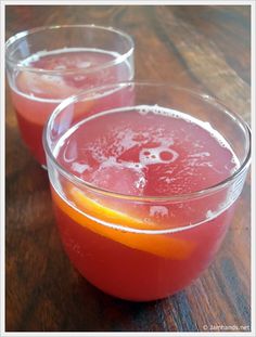 two glasses filled with red liquid sitting on top of a wooden table next to each other