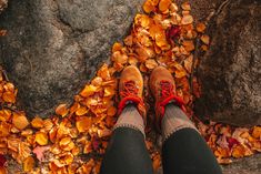 a person with red shoes standing on leaves in front of some rocks and trees,