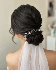 a bride with her hair in a low bun wearing a veil and flowers on the side