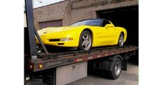 a yellow sports car is on the back of a flatbed truck in front of a brick building