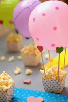 some pink and purple balloons are in small cupcakes on a blue table cloth