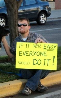 a man sitting on the curb with a dog holding a sign that says if it was easy everyone would do it