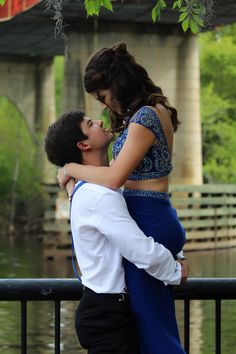 a young man and woman embracing each other in front of a river under a bridge