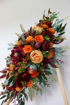 a bridal bouquet with orange and red flowers on a wooden stick in front of a white wall