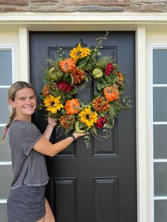 a woman is holding a wreath with flowers on it and standing in front of a door