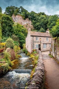 a river running through a lush green forest next to a stone building with windows on the side