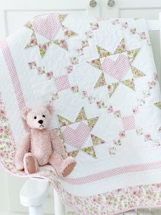 a pink teddy bear sitting on top of a quilt