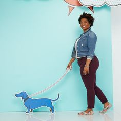 a woman with a dog on a leash standing in front of a blue wall and clouds