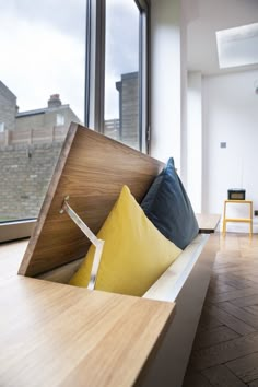 a wooden bench with pillows on it in front of a large window overlooking the city