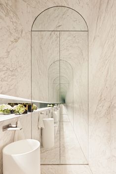 a bathroom with white marble walls and flooring, along with two urinals