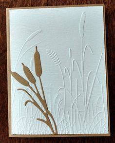 a close up of a card on a wooden surface with grass and reeds in the background