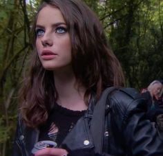 a woman with blue eyes is standing in the woods