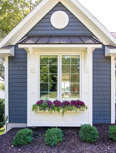 a blue house with white trim and two windows filled with flower boxes on the side