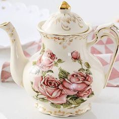 a white tea pot with pink roses on it and gold trimming around the top