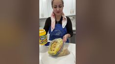 a woman in an apron preparing food on top of a kitchen counter next to a jar of mustard