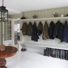 a coat rack filled with coats next to a wooden table and lamp hanging from the ceiling