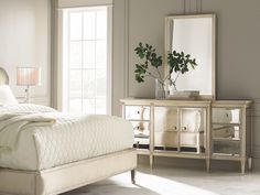 a white bed sitting next to a window in a bedroom under a large framed mirror