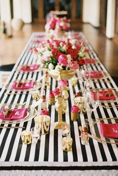 the table is set with black and white striped linens, pink napkins, gold plates, and flowers