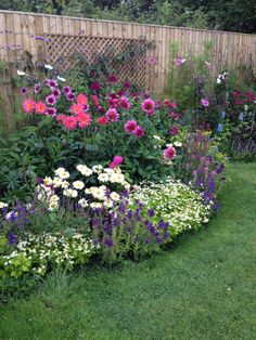 a garden filled with lots of colorful flowers next to a wooden fence and green grass