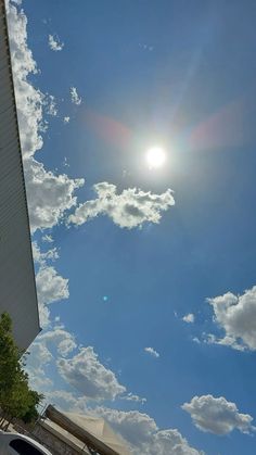 the sun shines brightly through the clouds in the blue sky over a building and parked cars