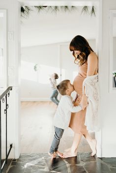 a woman holding onto a child's leg as they walk through an open door