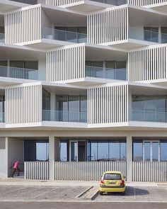 a yellow car parked in front of a tall building with balconies on it