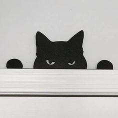 a black cat peeking out from behind a white mantle