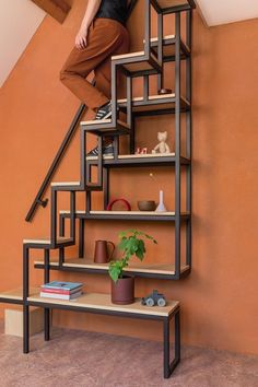 a woman standing on top of a stair case next to a potted plant and bookshelf