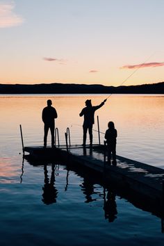 three people standing on a dock with a fishing rod in the water at sunset or dawn